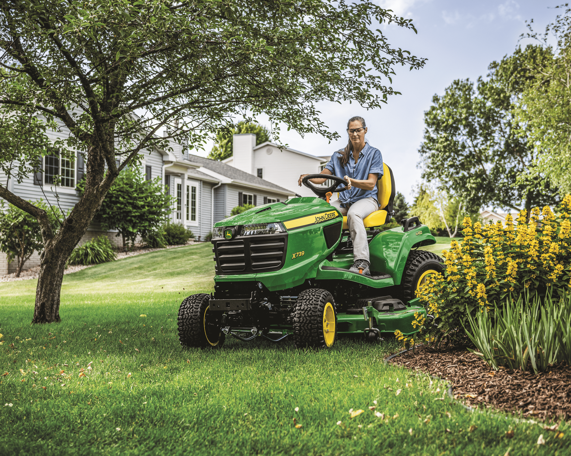 A female worker is riding a John Deere X739 Mower and mowing lawns